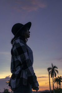 Rear view of woman standing against sky at sunset