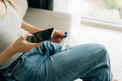 A woman is writing a chat message on her phone while holding a pregnancy test.