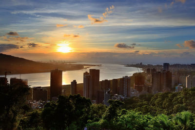 Cityscape by sea against sky during sunset