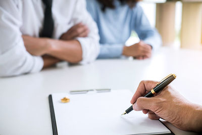 Cropped hand of lawyer signing divorce paper by couple sitting on desk