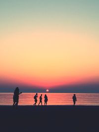 Silhouette people on beach against sky during sunset