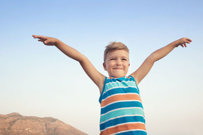 Smiling boy with arms outstretched standing against clear sky