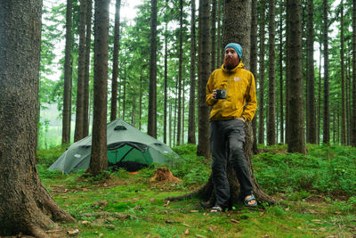 Smiling young man with coffee standing in forest