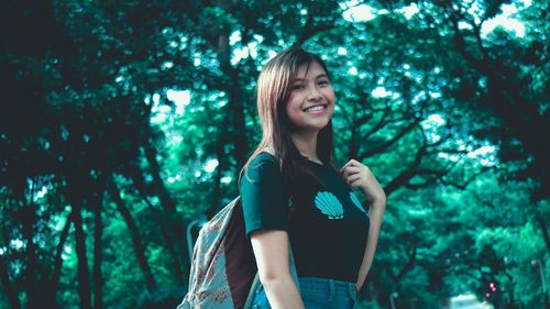 Portrait of smiling young woman standing against trees in forest