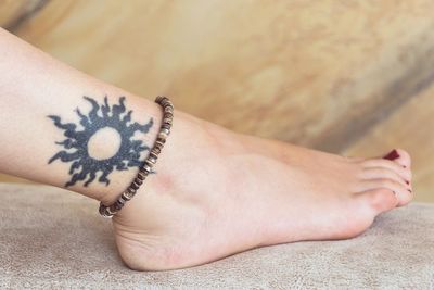 Low section of mid adult woman with tattoo wearing anklet