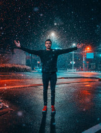 Full length of man with arms outstretched standing on street during snowfall