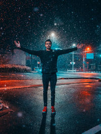 Full length of man standing on wet street at night