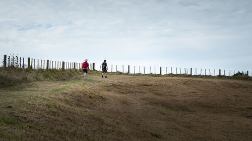 Rear view of people walking on field against sky