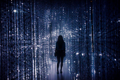 Silhouette of woman standing on walkway amidst illuminated beaded curtains