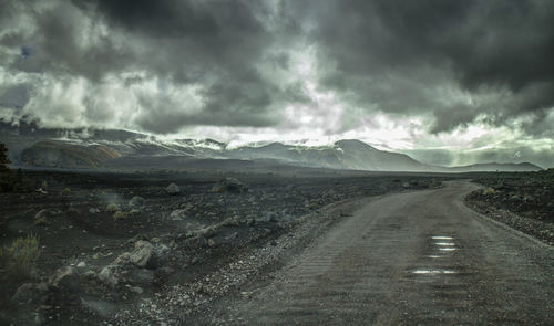 Road passing through landscape against storm clouds