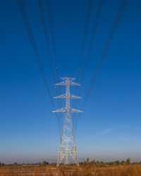 Electric pole and electric cable on the field in the countryside with blue sky.