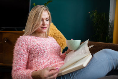 A girl reads a book with a cup in her hand while resting.