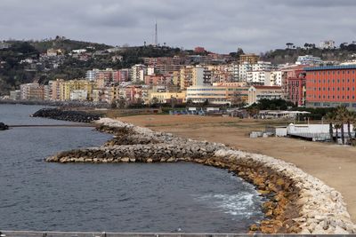 Sea by buildings in town against sky