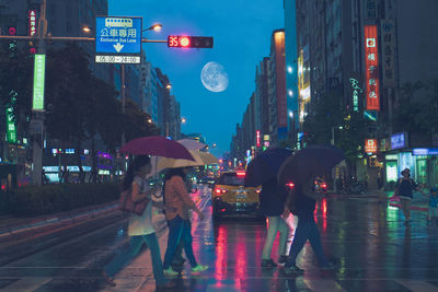 People walking on wet road in city during rainy season