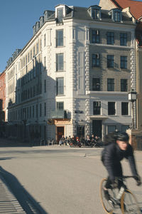 Blurred motion of people riding bicycle on road by buildings