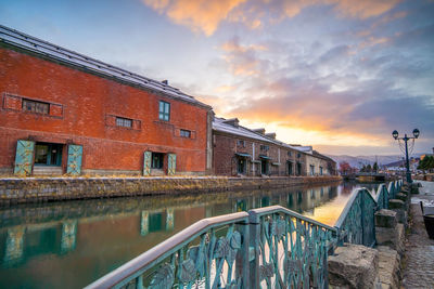 Bridge over canal by buildings against sky during sunset