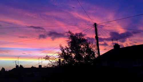 Low angle view of silhouette electricity pylon against dramatic sky