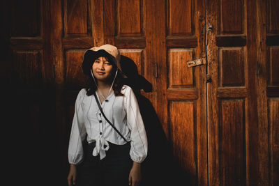 Young woman looking away while standing on wooden door