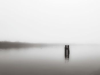 Wooden posts in lake against sky