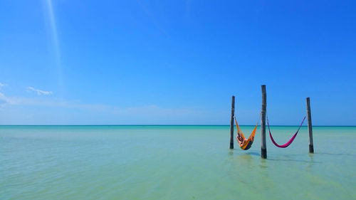 Woman relaxing in hammock at sea against sky