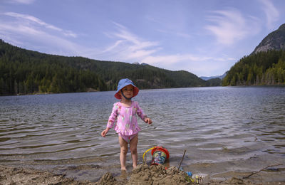 Full length of smiling girl standing by lake against sky