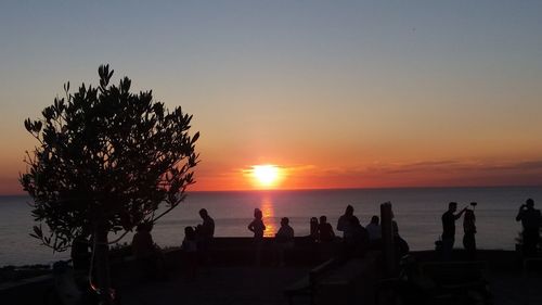 Silhouette people on beach against sky during sunset