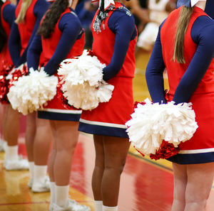 Cheerleaders standing in front of the bleachers with their pom poms behind them indoor.