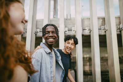 Happy teenage boys talking with female friend while walking near fence