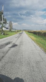 Road passing through field against cloudy sky