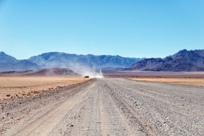 Dirt road in desert against clear sky