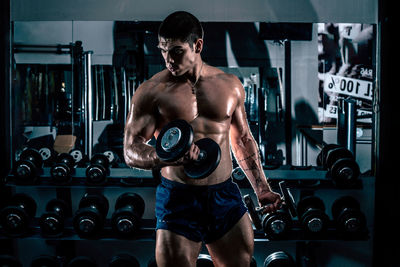 Shirtless man exercising with dumbbell at gym
