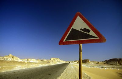 Low angle view of road sign against clear blue sky