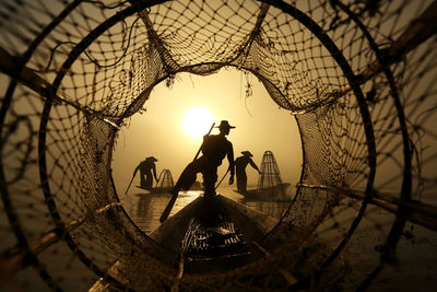 Silhouette fishermen standing on fishing boat against sky during sunset