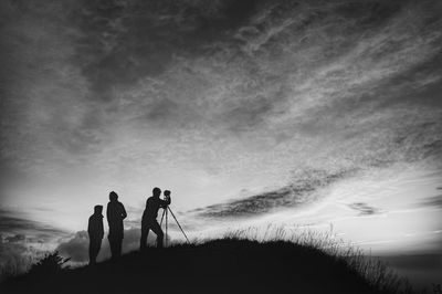 Silhouette friends photographing on mountain against sky