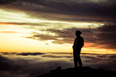 Silhouette man standing on rock against sky during sunset