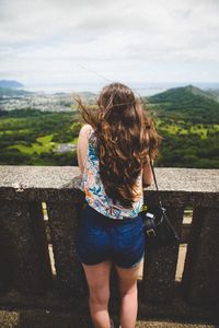 Rear view of woman leaning on railing against landscape