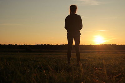 Silhouette woman standing on field against sky during sunset