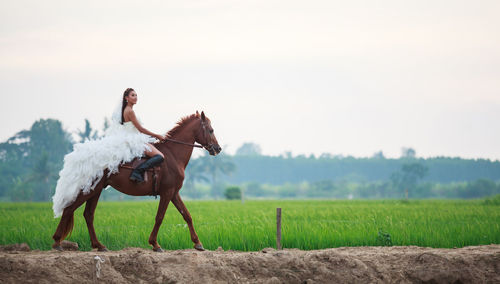 Side view of bride riding horse on field against clear sky