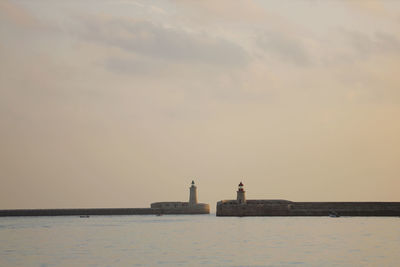 Lighthouse by sea against sky during sunset