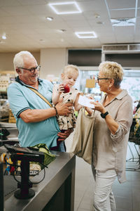 Girl assisting grandparents standing near checkout counter in supermarket