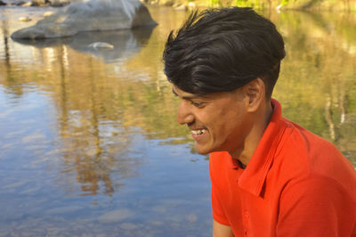Portrait of indian young man looking away in lake,  young guy smiling with sitting in riverside.