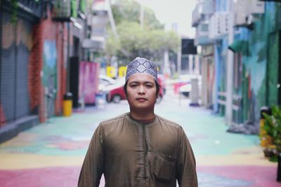 Portrait of young man wearing hat standing against city