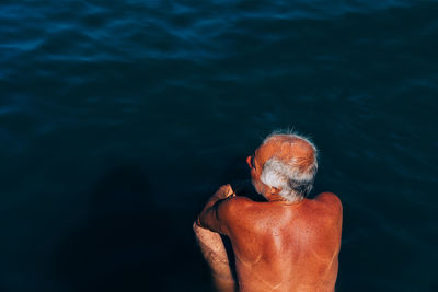 Rear view of shirtless man crouching by sea