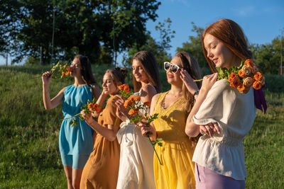 Smiling beautiful women holding flowers standing at park