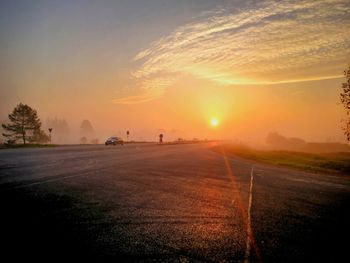 Road amidst field against sky during sunset