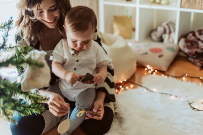 Mother playing with baby by christmas tree at home