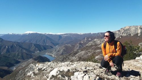 Full length of woman crouching on cliff against clear sky