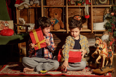 Two real brothers lie in a room with new year's decor near an armchair and look at gifts