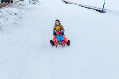 Wide angle view of two girls going down snow hill on sled one child closes eyes with hands