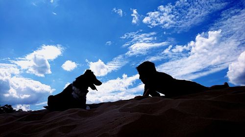 Silhouette of dog sitting against clouds